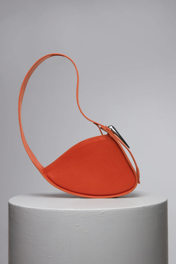 orange leather handbag with metal accessories on grey stand