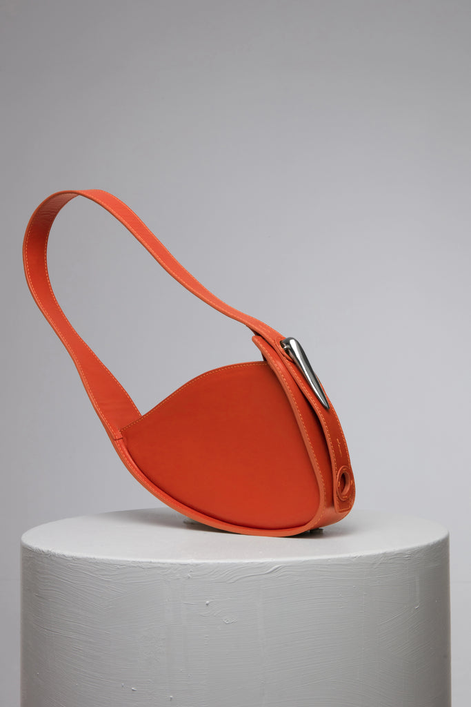 orange leather handbag with metal accessories on grey stand