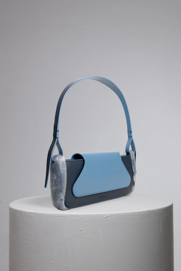 Blue geunine calf leather woman baguette bag on grey cylinder stand