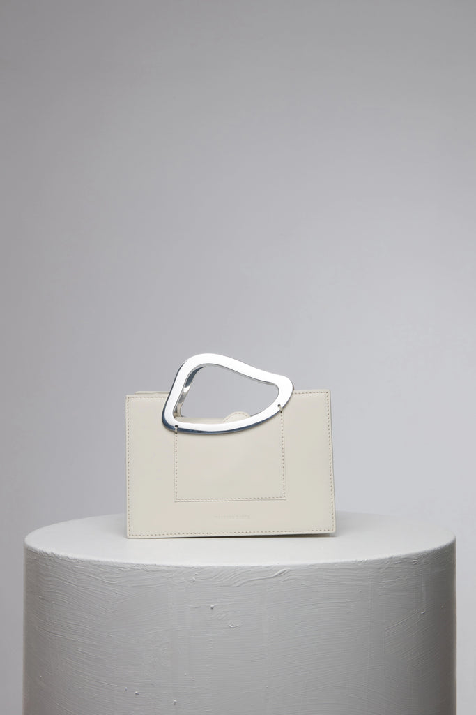rectangular white geunine leather handbag with metal top handle on white stand