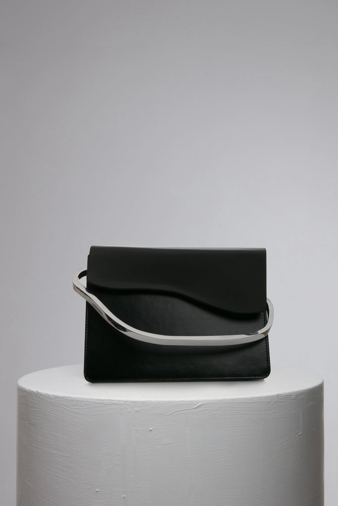 rectangular black leather handbag with metal top handle on white stand