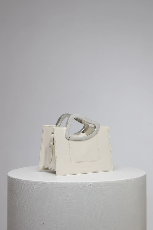 rectangular white geunine leather handbag with metal top handle on white stand