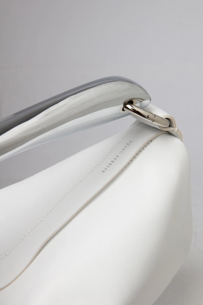White leather soft handbag with metal handle on a white stand