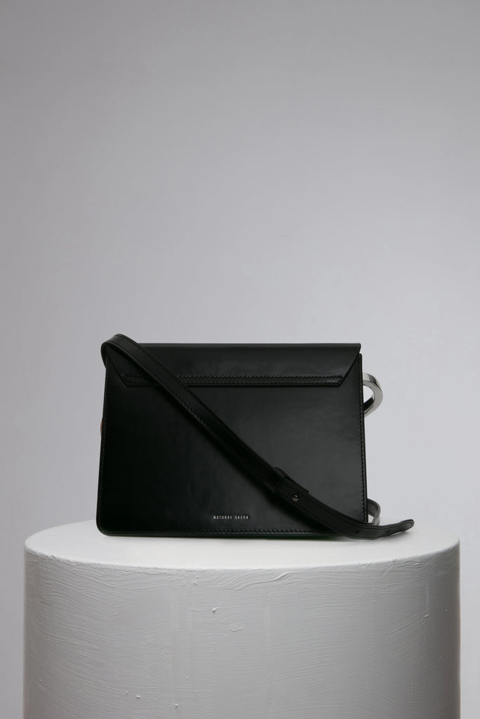 rectangular black leather handbag with metal top handle on white stand
