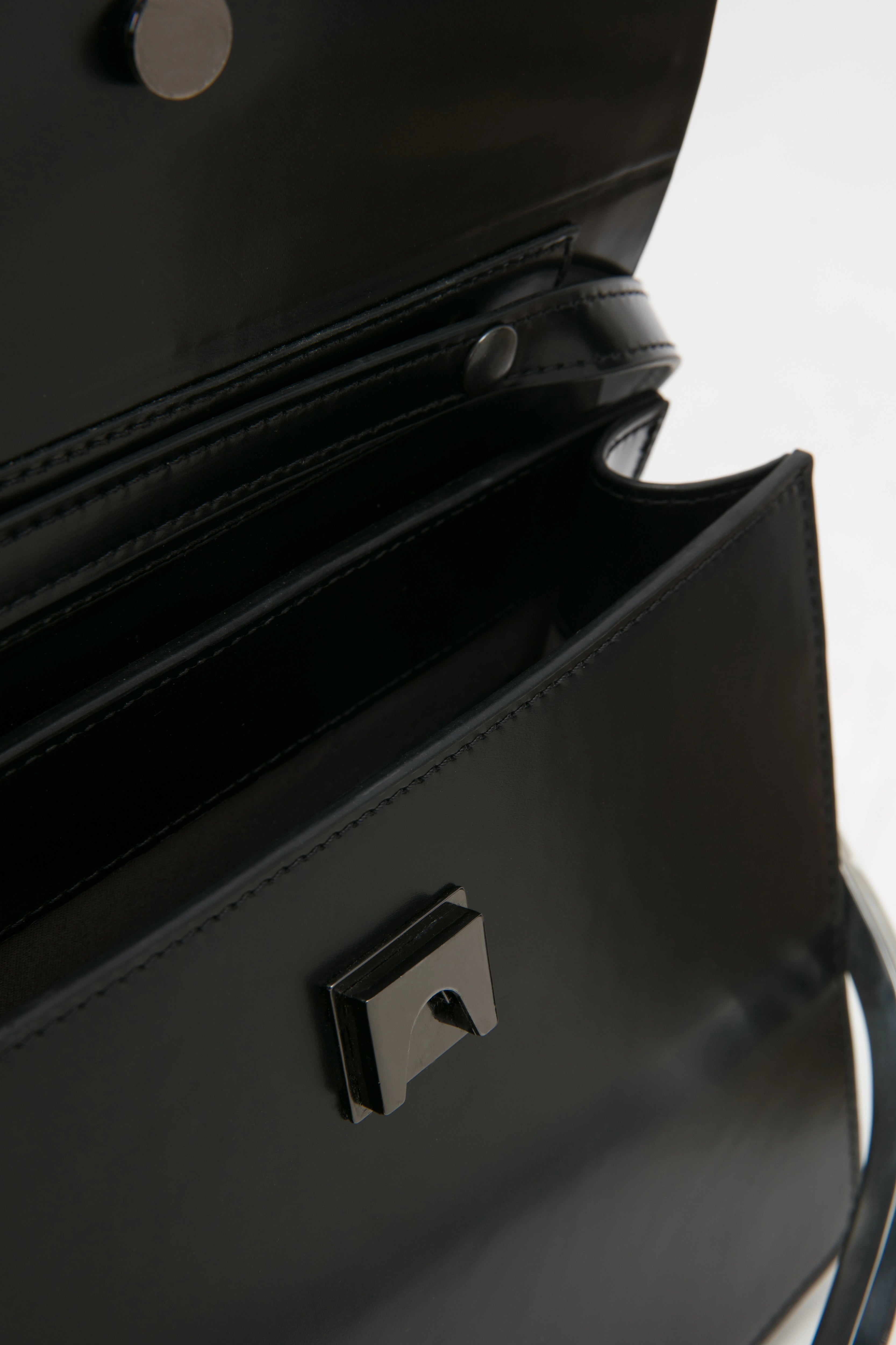 rectangular black leather handbag with metal top handle on white stand