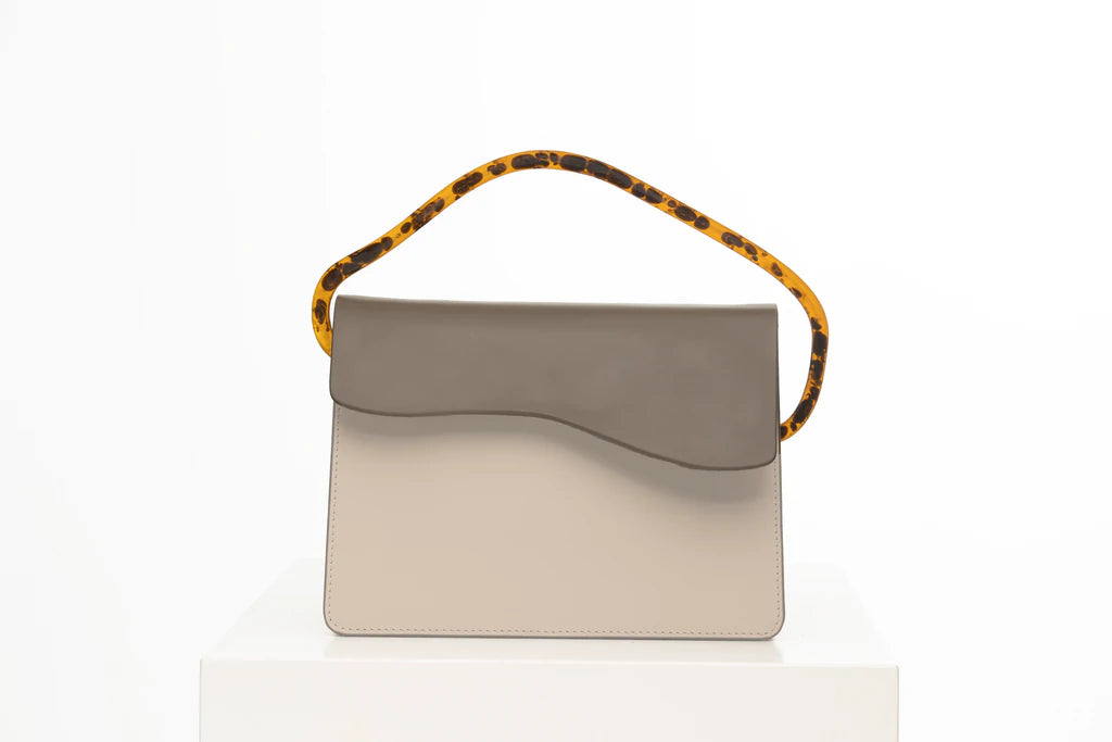 Rectangular women's bag with a taupe  genuine leather body and beige flap, bio resin handle and long shoulder handle, on a white stand in the studio
