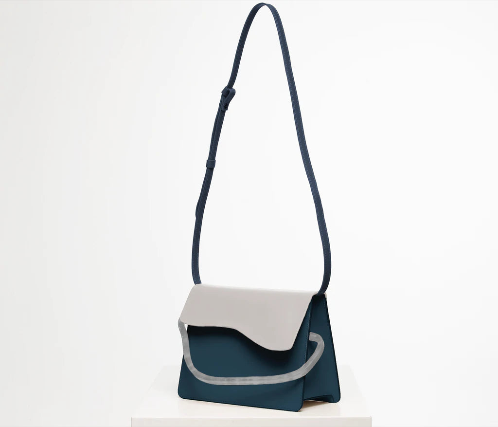 Rectangular women's bag with a blue genuine leather body and bianco flap, bio resin handle and long shoulder handle, on a white stand in the studio