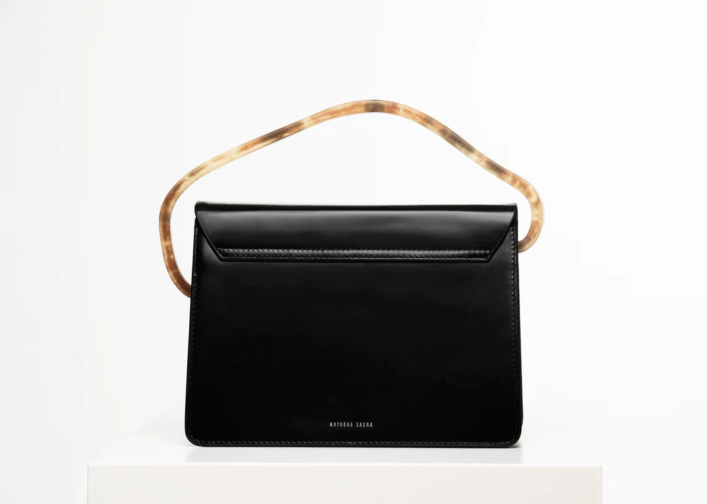Rectangular women's bag with a black genuine leather body and black flap, bio resin handle and long shoulder handle, on a white stand in the studio