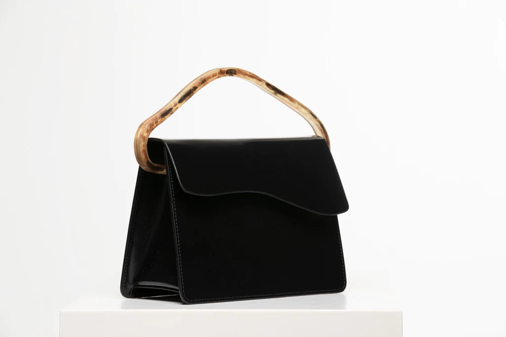 Rectangular women's bag with a black genuine leather body and black flap, bio resin handle and long shoulder handle, on a white stand in the studio