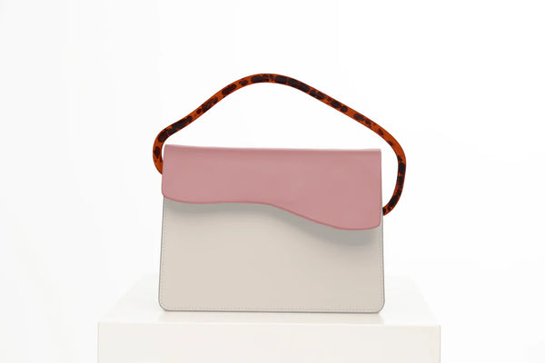 Rectangular women's bag with a bianco genuine leather body and dusty rose flap, bio resin handle and long shoulder handle, on a white stand in the studio