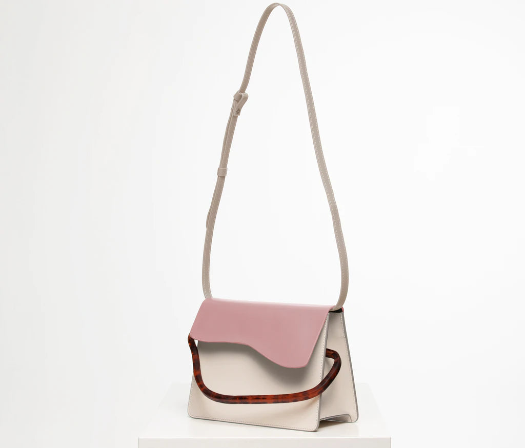 Rectangular women's bag with a bianco genuine leather body and dusty rose flap, bio resin handle and long shoulder handle, on a white stand in the studio