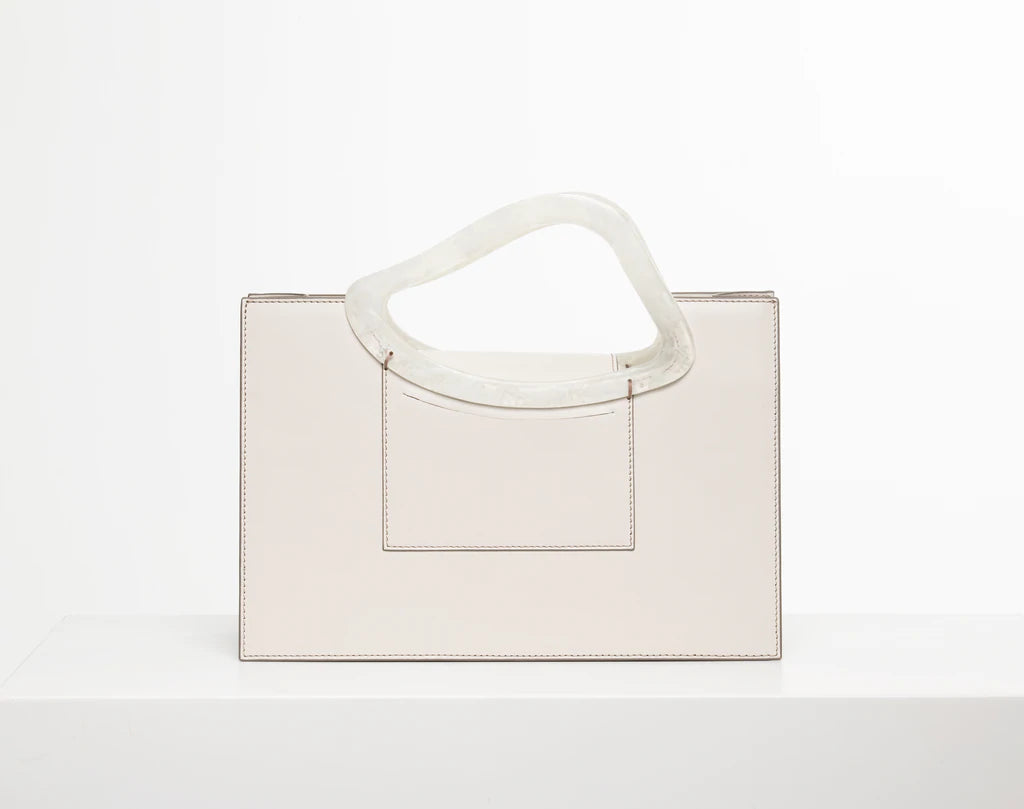 Off white calf leather medium structured rectangle bag with bio resin handle and removable calf leather shoulder strap on a white stand