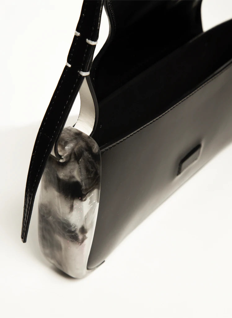 Black calf leather mini rectangle boguette bag with special resin cover companents on the sides. non-removable shoulder strap on a white stand