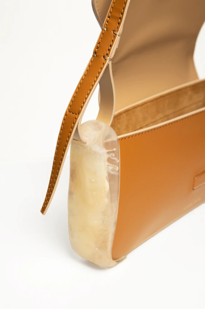 Oyster calf leather rectangle baguette bag with special resin cover companents on the sides. non-removable shoulder strap on a white stand