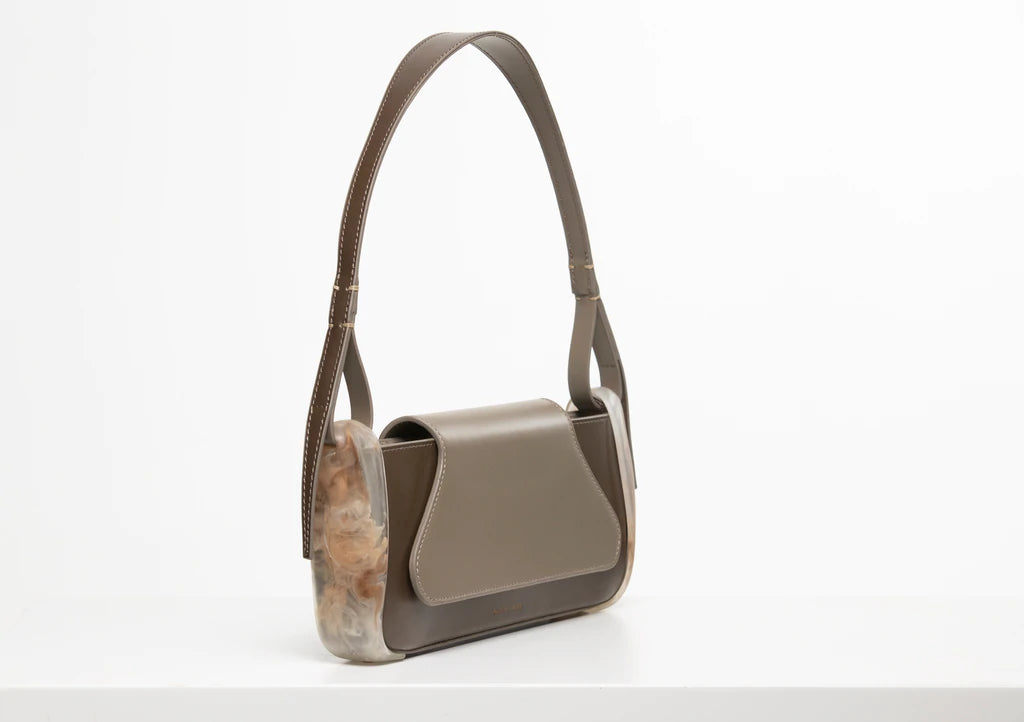 Taupe calf leather rectangle baguette bag with special resin cover companents on the sides. non-removable shoulder strap on a white stand