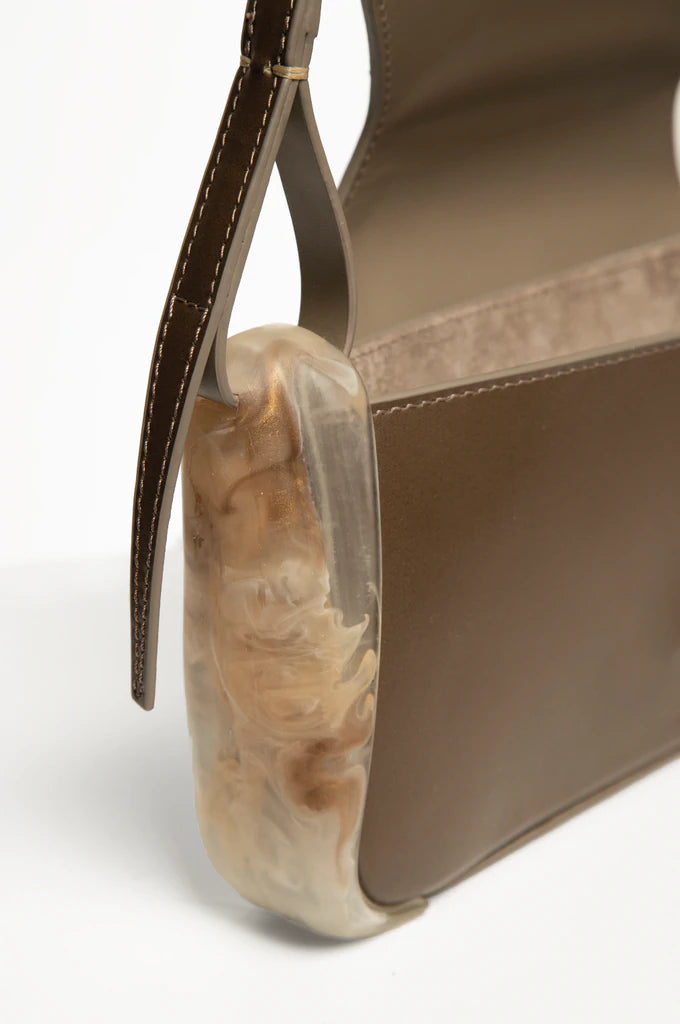 Taupe calf leather rectangle baguette bag with special resin cover companents on the sides. non-removable shoulder strap on a white stand