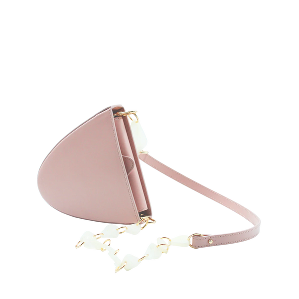 Flap topped oval structured dusty rose calf leather cross body bag with an adjustable leather and natural resin chain linked strap on a white stand
