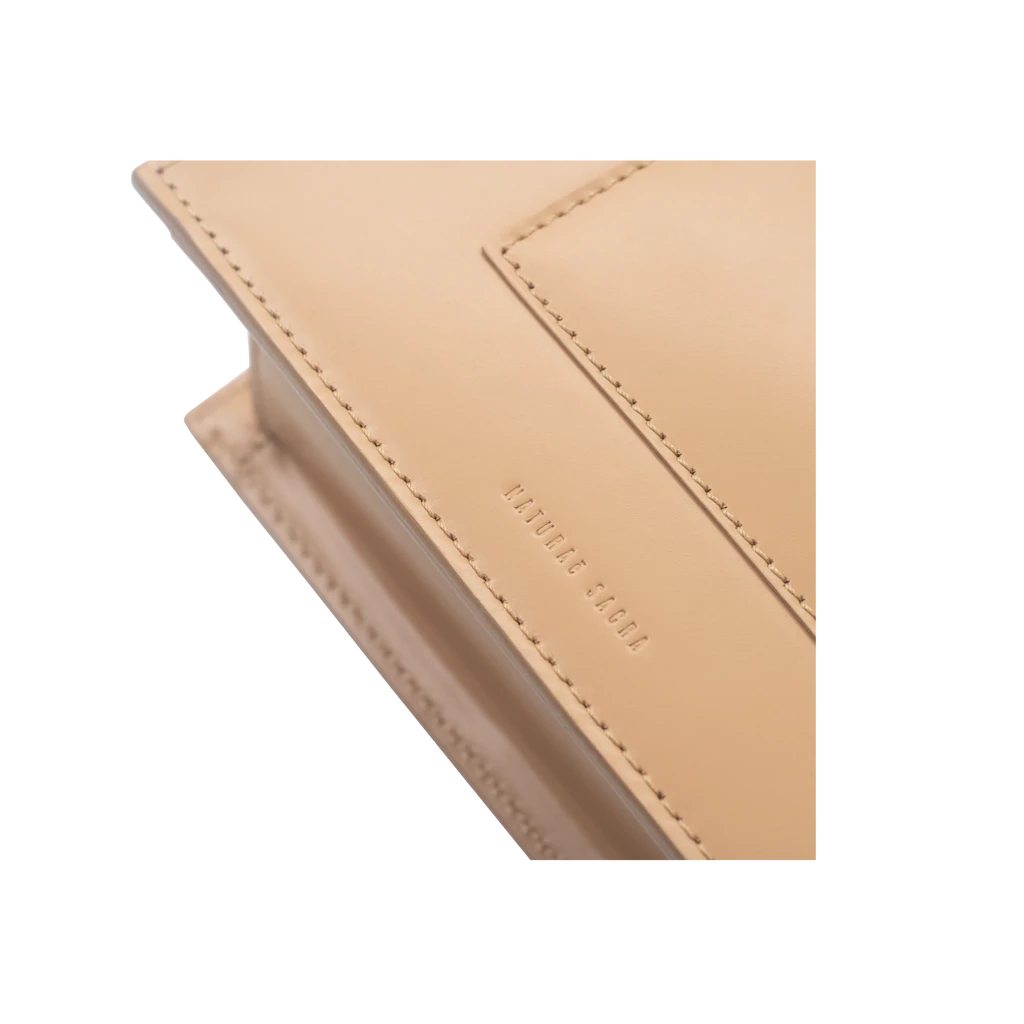 Rectangle shaped champagne calf leather saddle bag with natural resin handle holder and remowable calf leather handle strap on a white stand