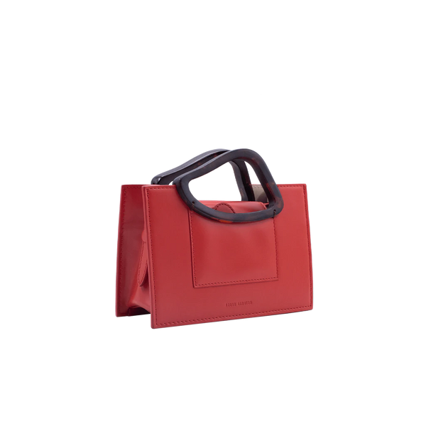 Rectangle shaped red calf leather saddle bag with natural resin handle holder and remowable calf leather handle strap on a white stand