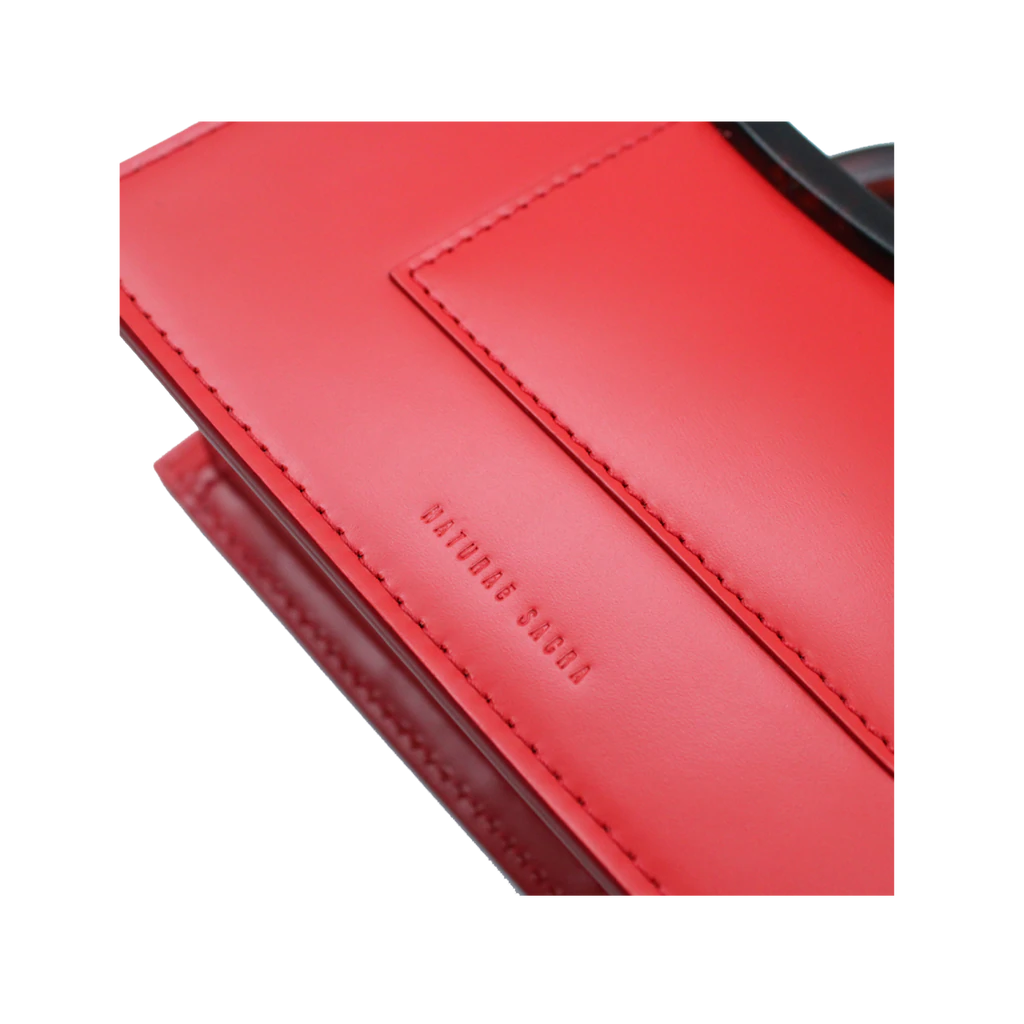 Rectangle shaped red calf leather saddle bag with natural resin handle holder and remowable calf leather handle strap on a white stand