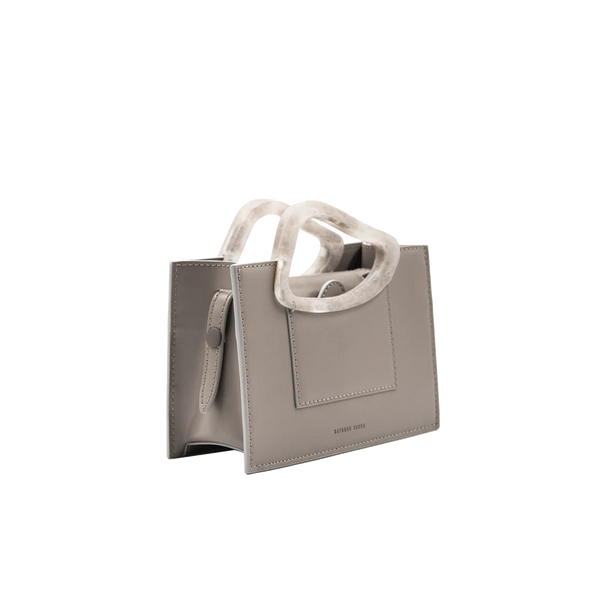 Rectangle shaped taupe calf leather saddle bag with natural resin handle holder and remowable calf leather handle strap on a white stand