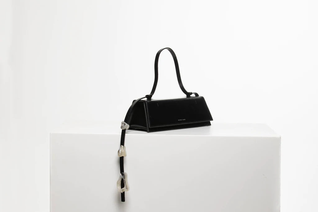 Rectangle shaped black calf leather clutch bag with natural resin filled in handles and removable calf leather handle strap on a white stand