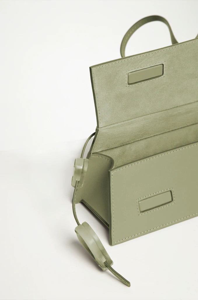 Rectangle shaped mint calf leather clutch bag with natural resin filled in handles and removable calf leather handle strap on a white stand