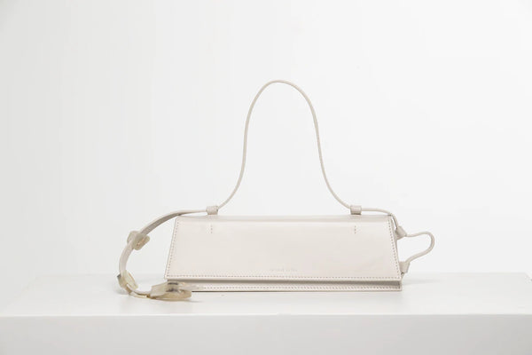 Rectangle shaped off white calf leather clutch bag with natural resin filled in handles and removable calf leather handle strap on a white stand