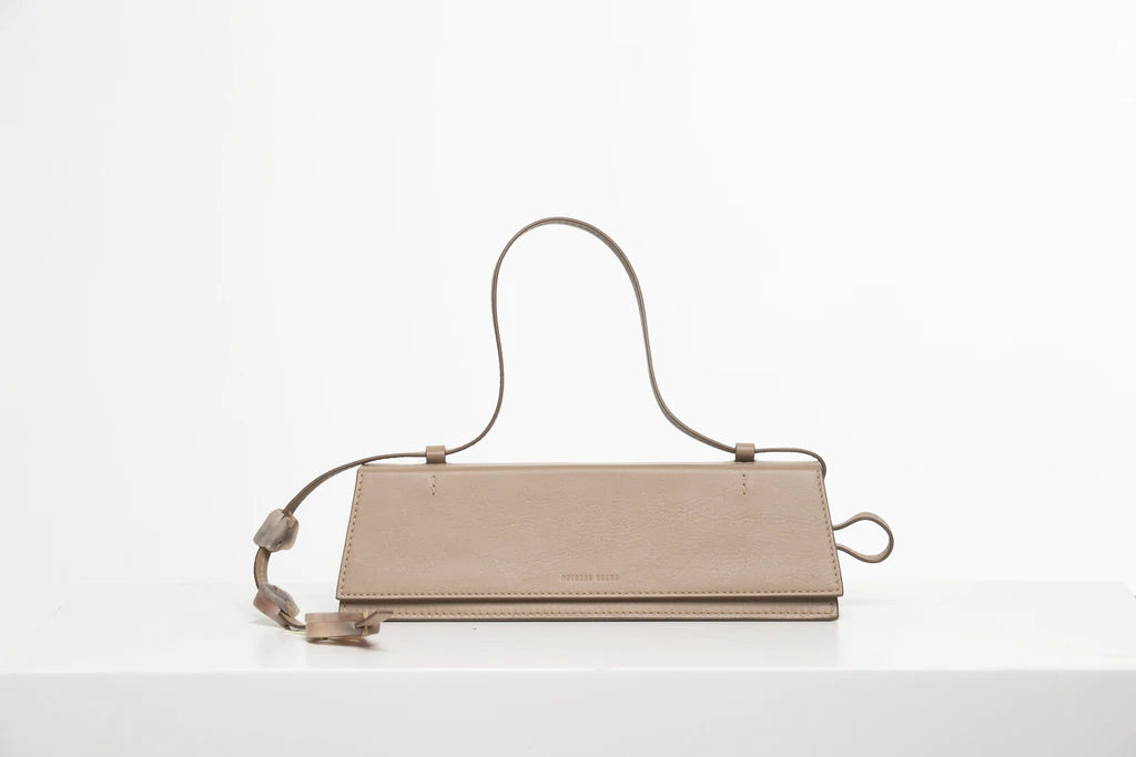 Rectangle shaped taupe calf leather clutch bag with natural resin filled in handles and removable calf leather handle strap on a white stand